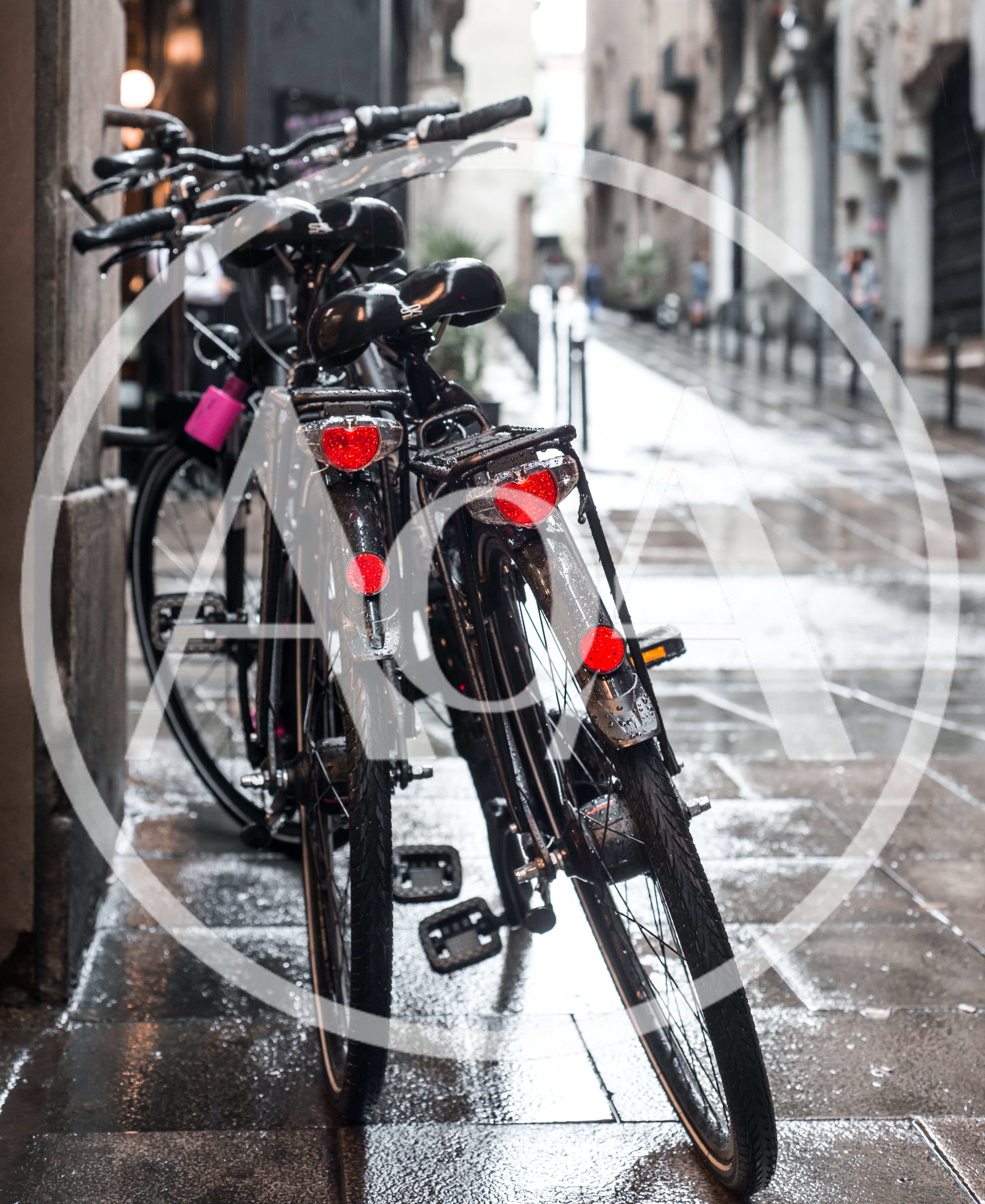 Two Black Bicycles Parked On A Wet City Street