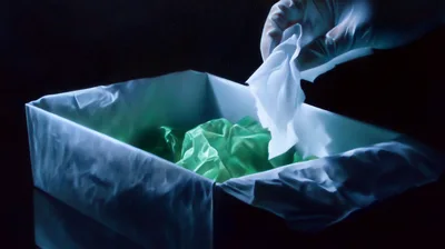 Gloved Hand Disposing Tissue Into Waste Bin