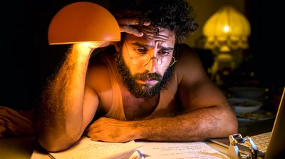 Stressed Man Working Late At Night Under Desk Lamp