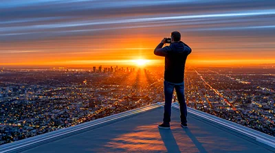 Photographer Standing On Rooftop Overlooking City At Sunset