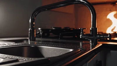 Kitchen Sink Faucet With Gas Stove Flames In Background