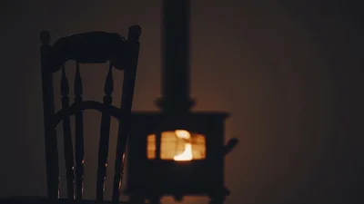 Silhouette Of A Wooden Chair Beside A Burning Wood Stove