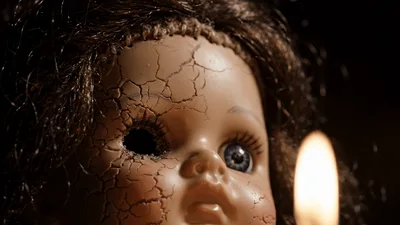 Creepy Cracked Doll Face Illuminated By Flickering Candle Light