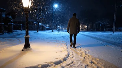 Man Walking Down Snowy Street At Night