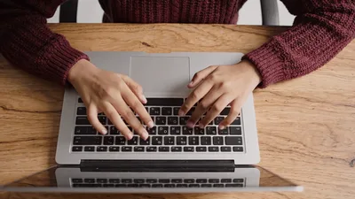 Young Woman Typing On Laptop At Wooden Desk