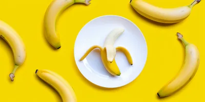 Peeled Banana On A White Plate Surrounded By Whole Bananas