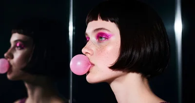 Young Woman With Glitter Makeup Blowing Pink Bubblegum