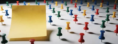 Yellow Sticky Note Surrounded By Colorful Push Pins