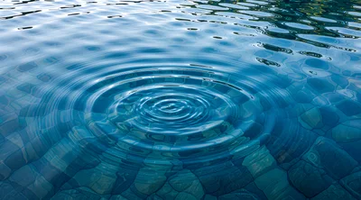 Concentric Ripples Expanding On Clear Blue Water Surface