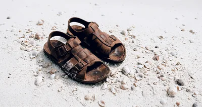 Brown Leather Sandals Resting On White Sandy Beach