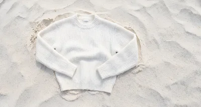 White Knitted Sweater Resting On Sandy Beach