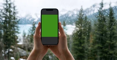 Person Holding Smartphone With Green Screen Against Rainy Window