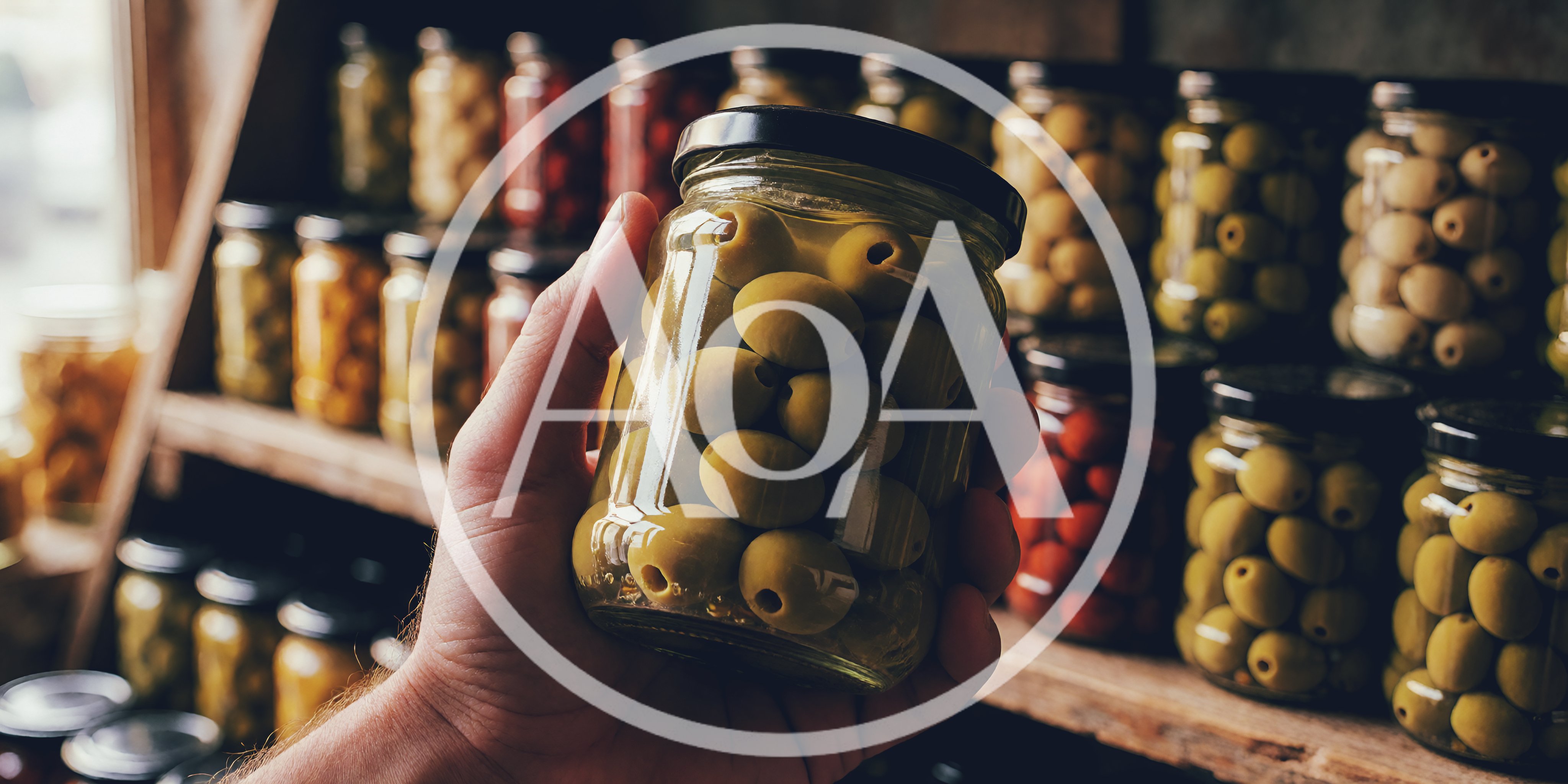 Hand Holding A Jar Of Green Olives In A Pantry