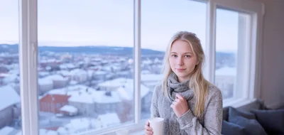 Young Woman Holding Coffee Mug By Snowy Window