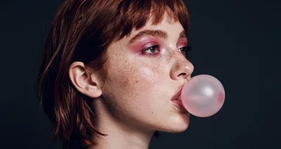 Young Woman With Freckles Blowing A Pink Bubblegum Bubble