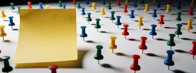Yellow Sticky Note Surrounded By Colorful Push Pins