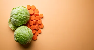 Fresh Cabbage Heads and Sliced Carrots on Orange Background