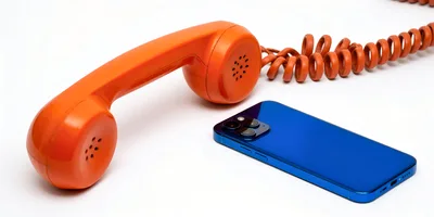 Vintage Orange Telephone Handset Beside Modern Blue Smartphone