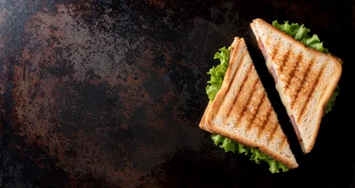 Two Grilled Ham and Cheese Sandwiches on Dark Surface