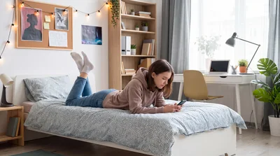 Teenager using a mobile phone while lying on a bed at home