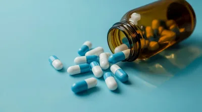 Blue and White Capsules Spilling From Amber Glass Bottle