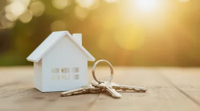 Miniature House Model With Metal Keys On Wooden Table