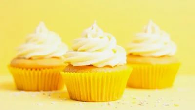 Three Vanilla Cupcakes With White Frosting On Yellow Background