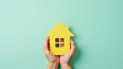 Hands Holding A Yellow Paper House Cutout