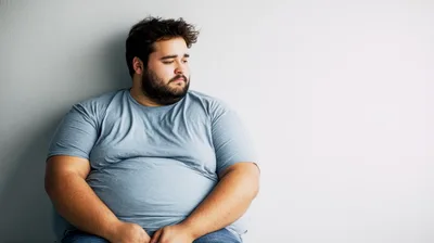 Overweight Man Sitting Alone Against A Grey Wall
