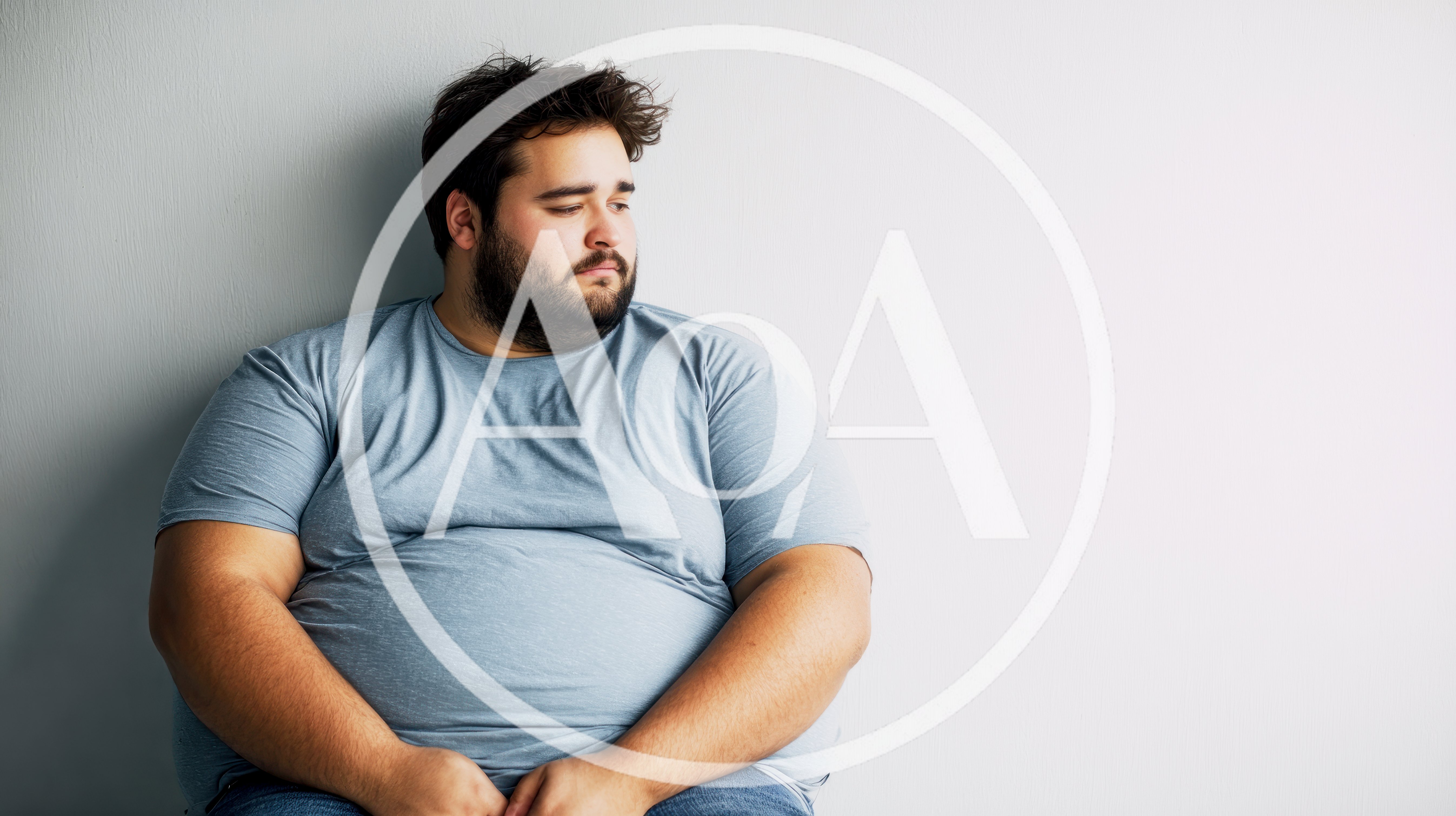 Overweight Man Sitting Alone Against A Grey Wall