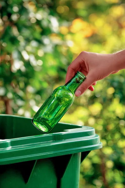 Hand Placing Green Glass Bottle Into Recycling Bin