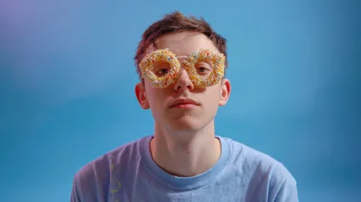 Young Man Wearing Donut Glasses Against Blue Background