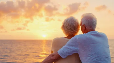 Elderly Couple Embracing While Watching Sunset Over Ocean