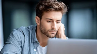 Pensive Young Man Working On Laptop In Office