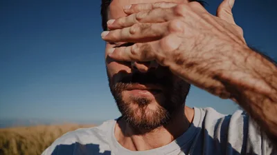 Man Shielding Eyes From Bright Sun In Field
