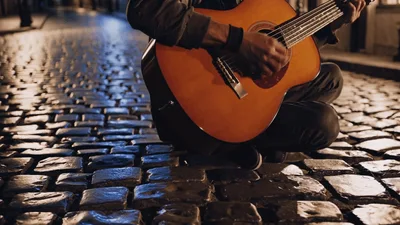 Street Musician Playing Acoustic Guitar On Cobblestone Street