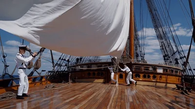 Sailors Hoisting White Sail On Wooden Tall Ship
