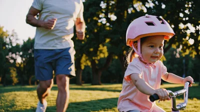 Father Jogging Behind Daughter Riding Her Bicycle In Park