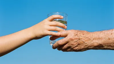 Young Hand Passing Glass of Water to Elderly Hand