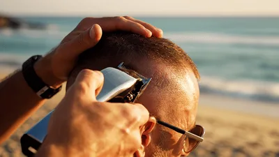 Barber Trimming Hair With Clippers On Beach