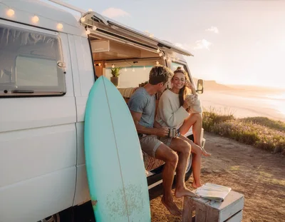 Couple Enjoying Coffee By Their Camper Van At Sunset