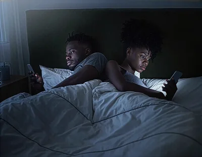 Young Couple Using Smartphones In Bed At Night