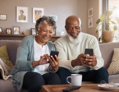 Senior Couple Using Smartphones Together On Sofa