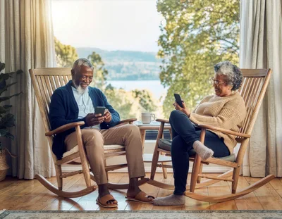 Senior Couple Relaxing In Rocking Chairs With Smartphones