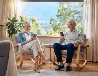 Senior Couple Using Smartphones In Living Room