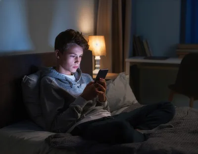 Teenage Boy Using Smartphone In Bed At Night