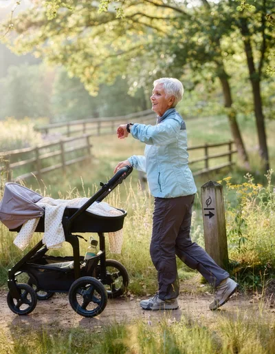 Senior Woman Walking With Baby Stroller In Park