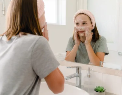 Teenage Girl Washing Face With Cleanser In Bathroom Mirror