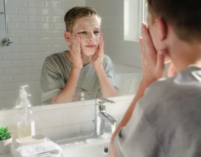 Young Boy Washing Face With Soap In Bathroom Mirror