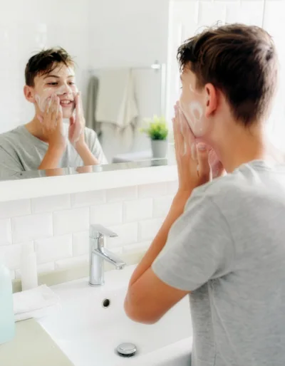 Teenage Boy Washing Face With Cleanser In Bathroom
